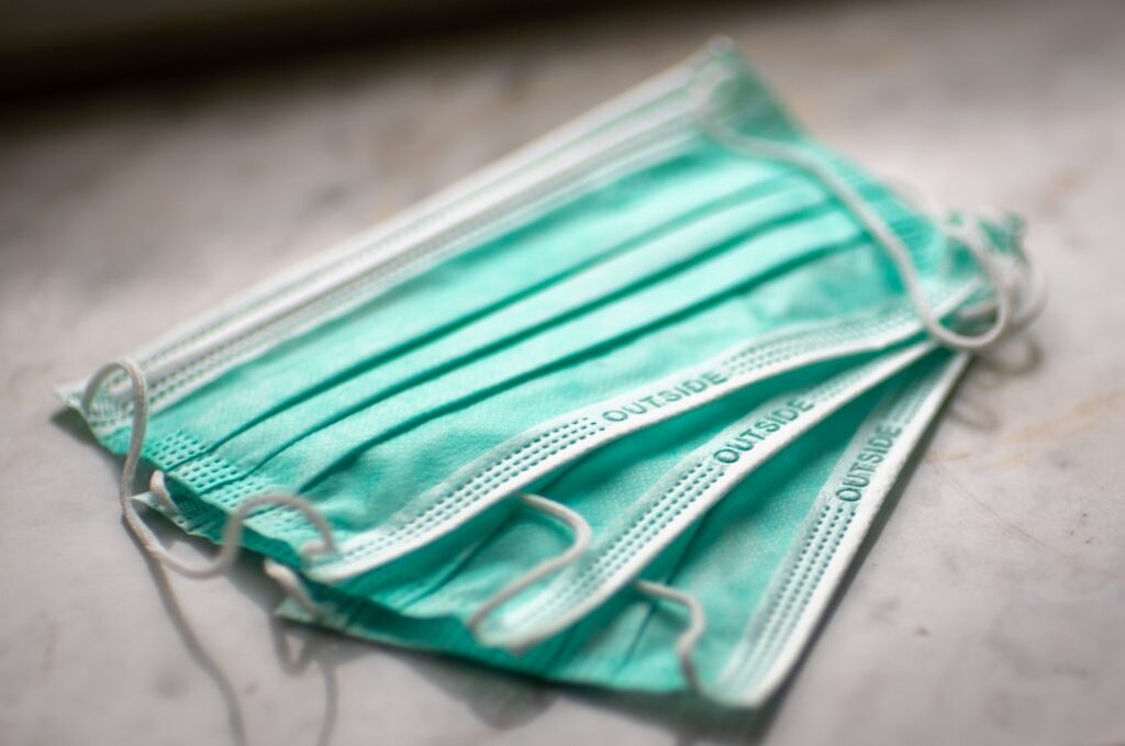 A healthcare worker wearing a surgical mask holds a counterfeit N95 mask box with a fake NIOSH approval label.
